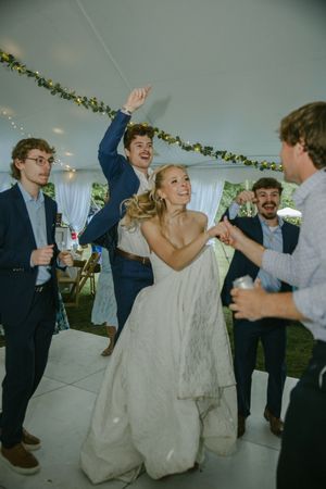 Wedding celebration in a tent with guests dancing and celebrating on the dance floor.
