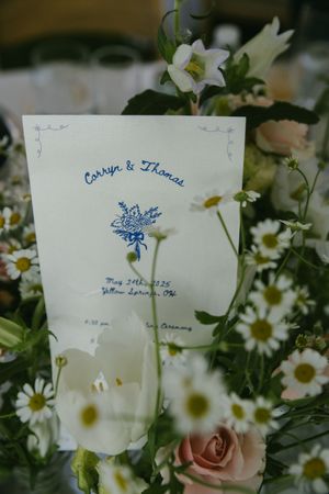 Wedding invitation cards displayed among white daisies and pink roses.