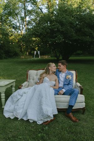Newlyweds share an intimate moment on a vintage sofa during their garden wedding reception.