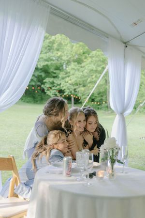 Wedding party leaning in for group photo at white-draped reception tent.