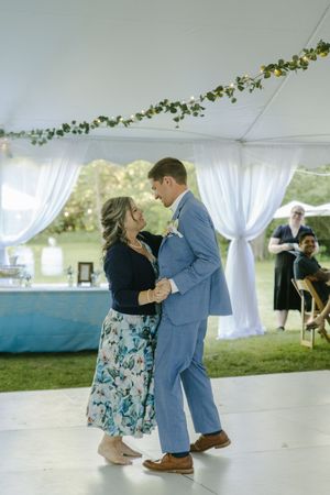 Couple dancing together under a white tent decorated with greenery and sheer drapes.
