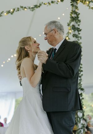 A special father-daughter dance moment under twinkling lights and greenery at a wedding reception.