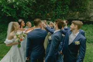 Wedding party celebrates outdoors with champagne sprays in a garden setting.