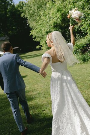 Wedding party poses playfully on a sunny lawn with flowing white dress and blue suits.
