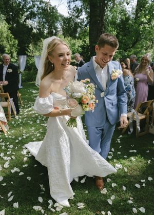Newlyweds walk through flower petals during outdoor garden ceremony.