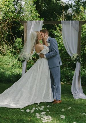 Romantic outdoor wedding ceremony with white drapes and flower petals scattered on green grass.