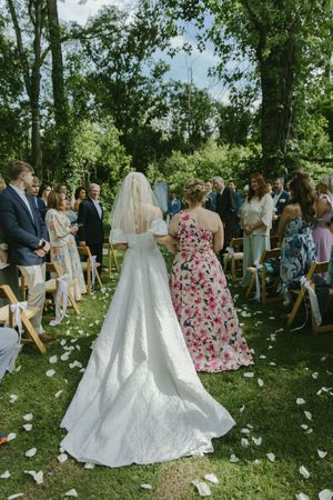 Wedding party and guests gather on lawn scattered with white flower petals.