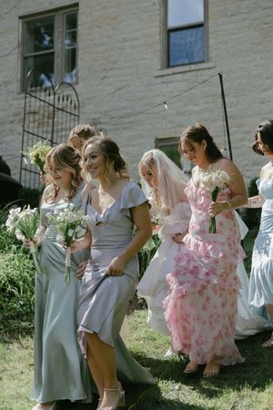 Bridesmaids in light colored and pink floral dresses laughing together outside a stone building.