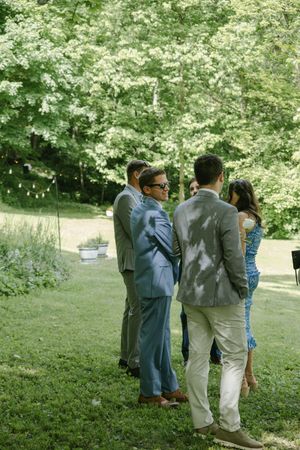 Wedding guests gather in casual conversation on a grassy hillside.