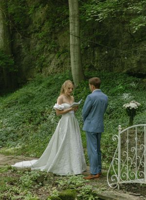 Bride and groom walk hand in hand along a romantic garden path with white iron gates.