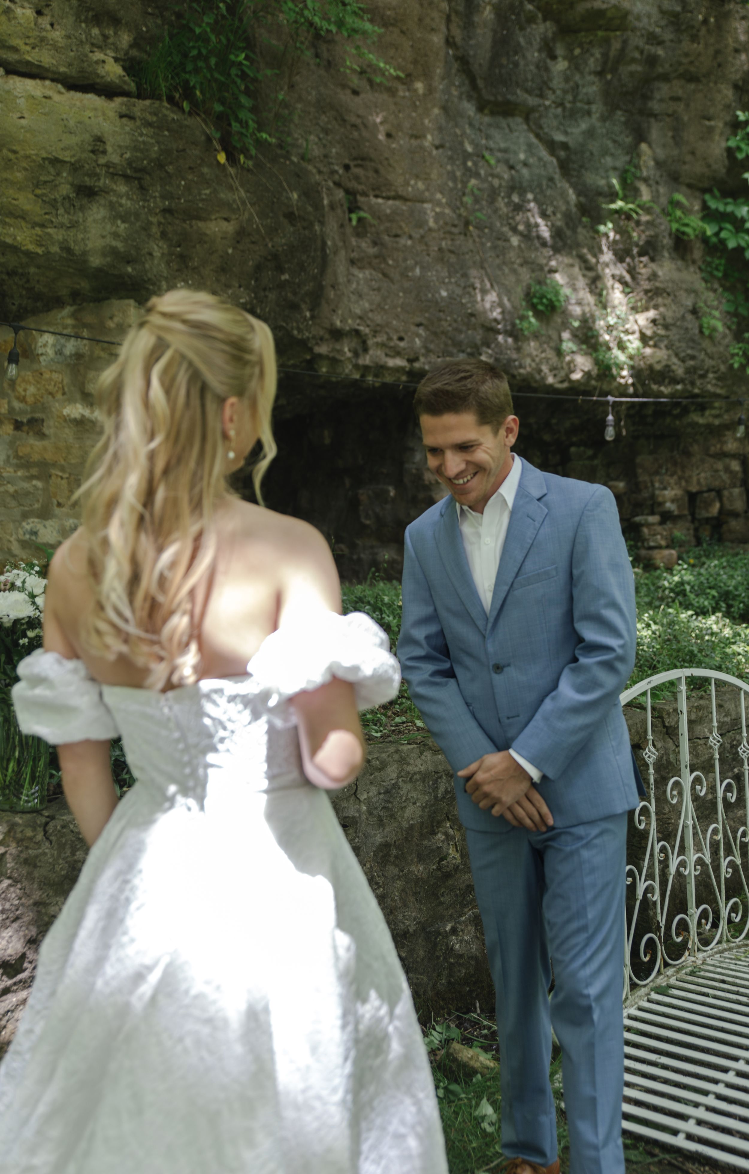 Romantic moment between couple by stone wall with decorative white garden bench.