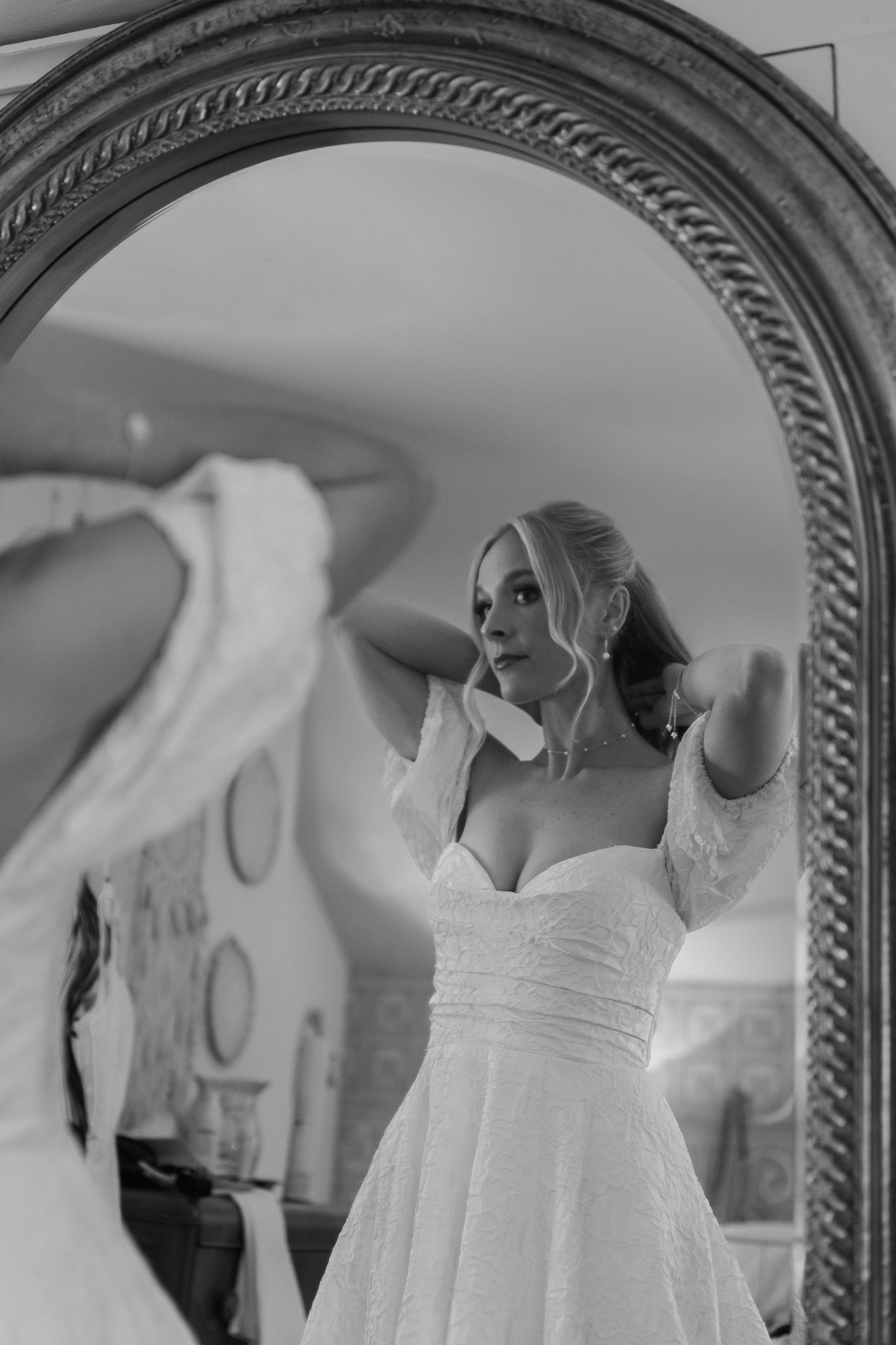 A white wedding dress displayed on a hanger against an ornate mirror frame.