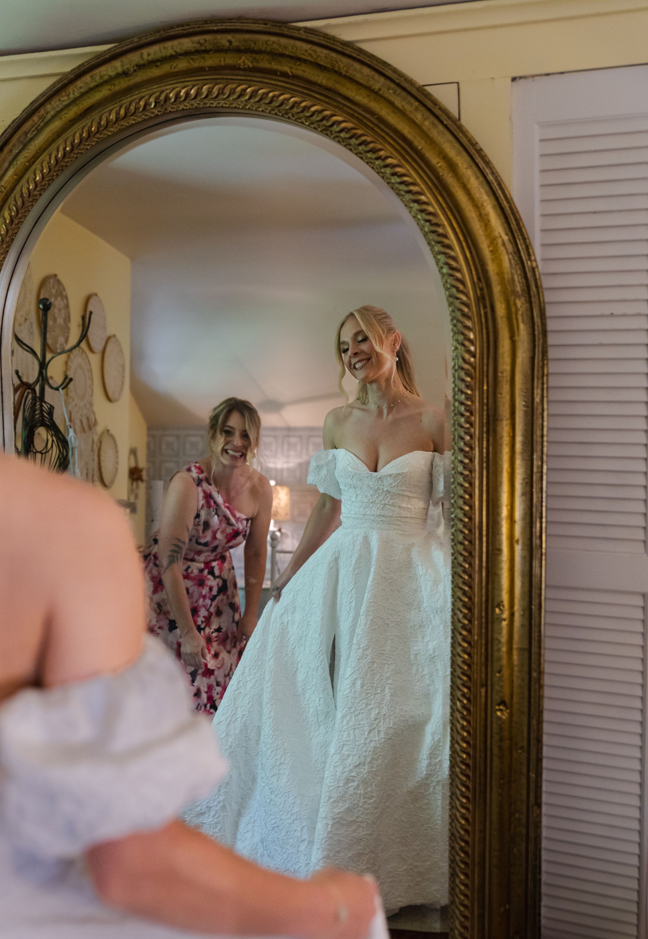 Elegant white wedding dress reflected in an ornate gold-framed mirror with decorative borders.