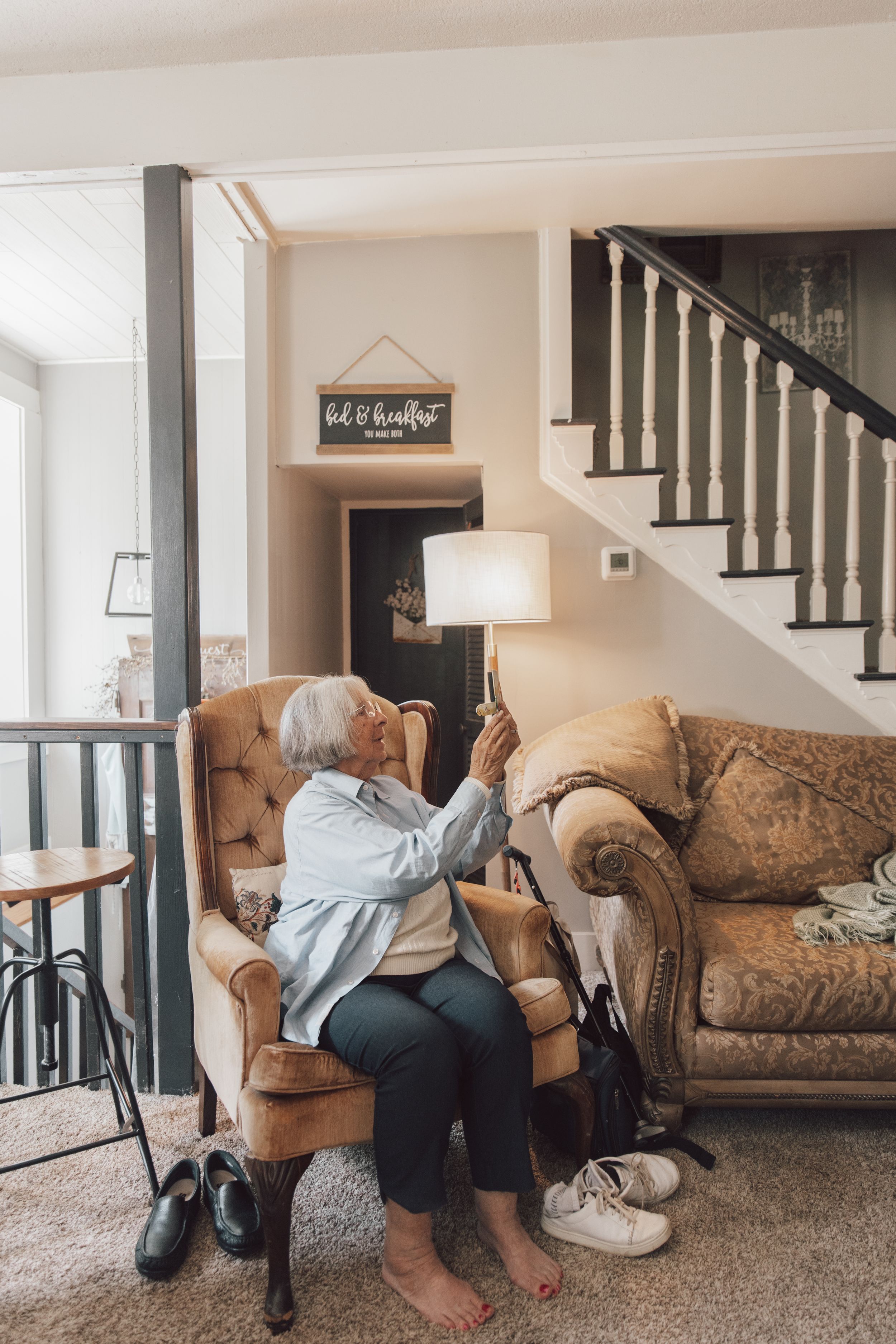 Living room scene with a brown patterned couch and black staircase railing visible.