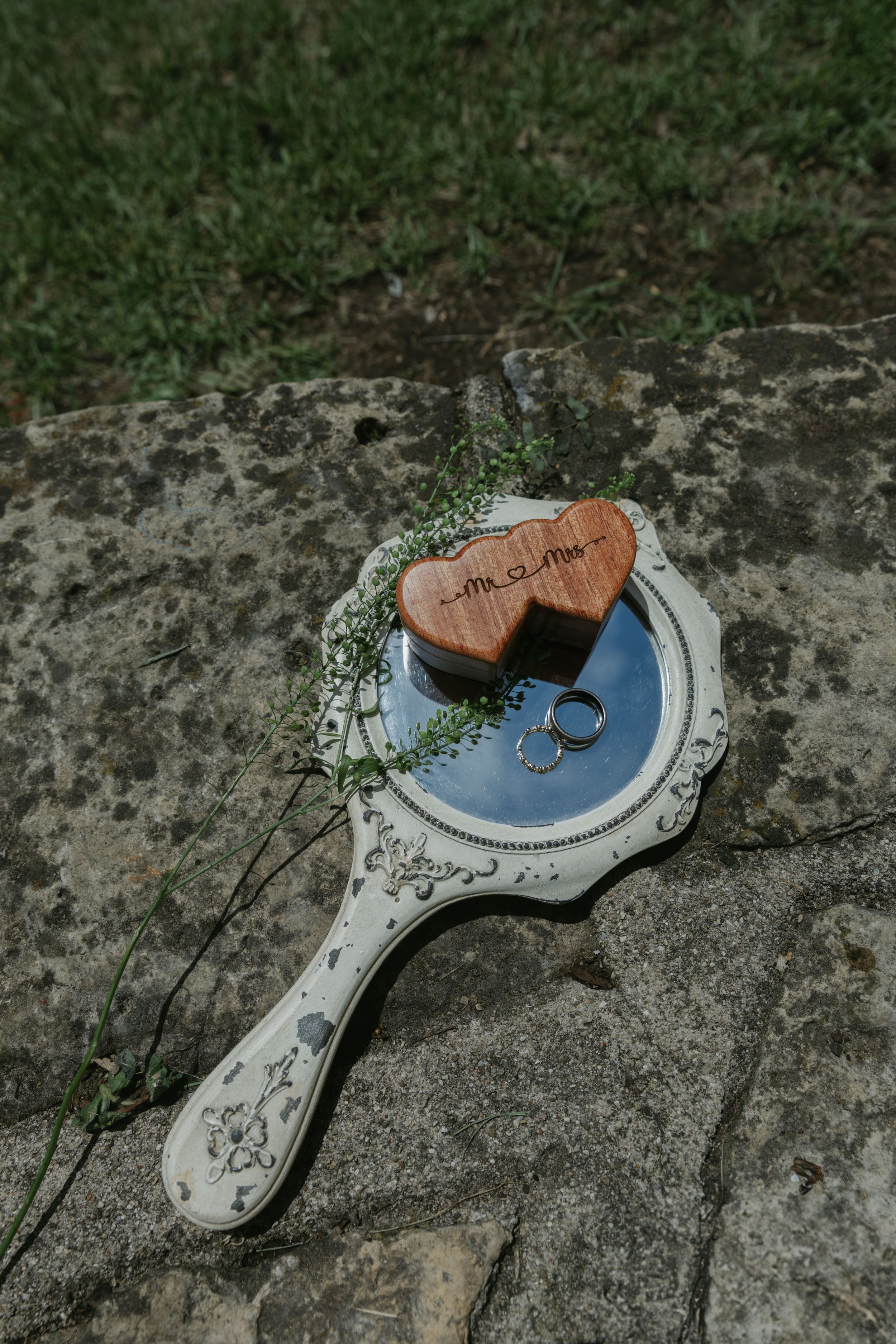 Vintage style ornate hand mirror with intricate details lies on a textured stone surface.