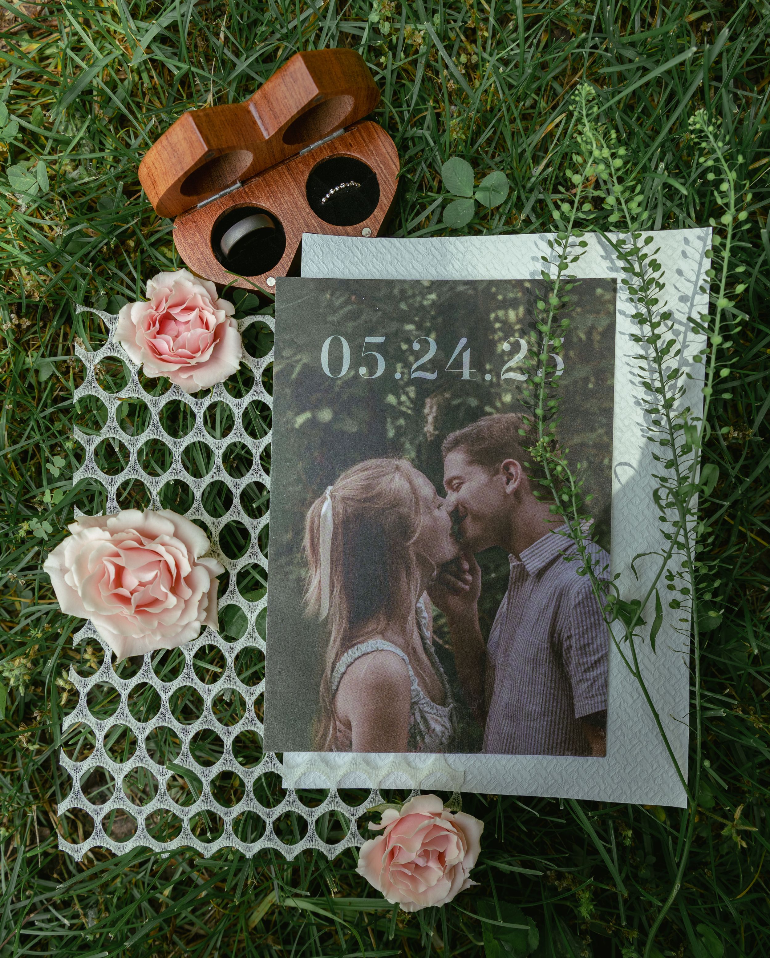 A wedding photograph is displayed on paper alongside pink roses and coffee cups on green grass.