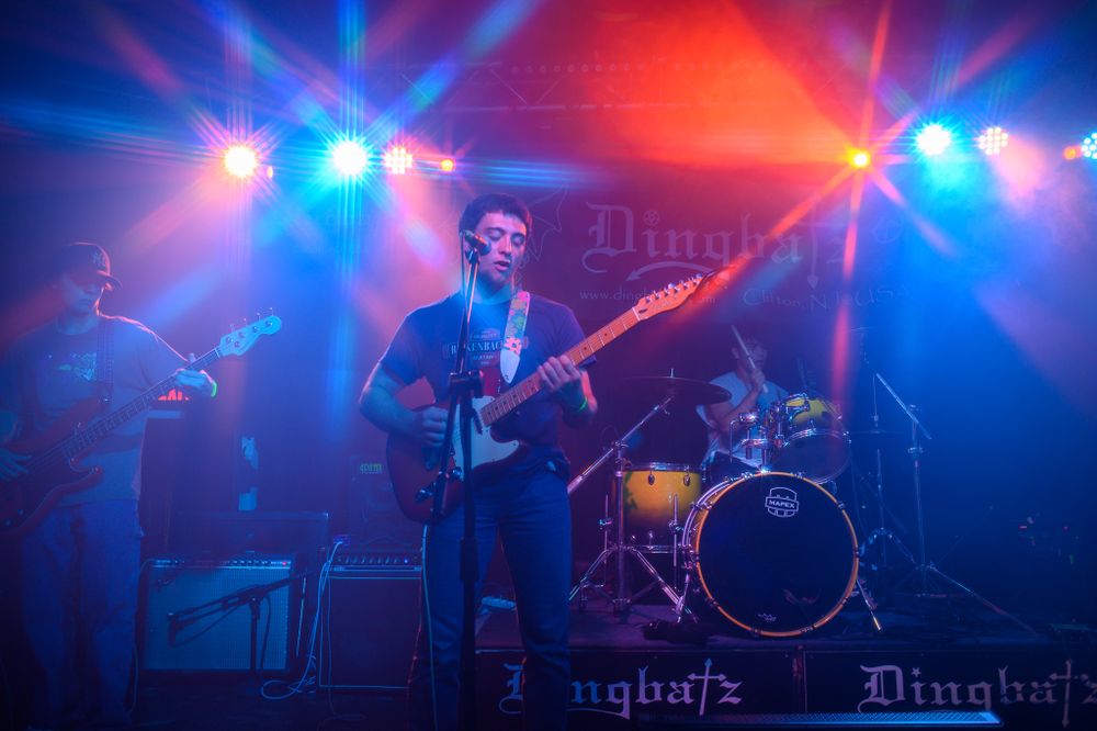 Musician performs on stage with electric bass guitar under dramatic blue and red concert lighting.