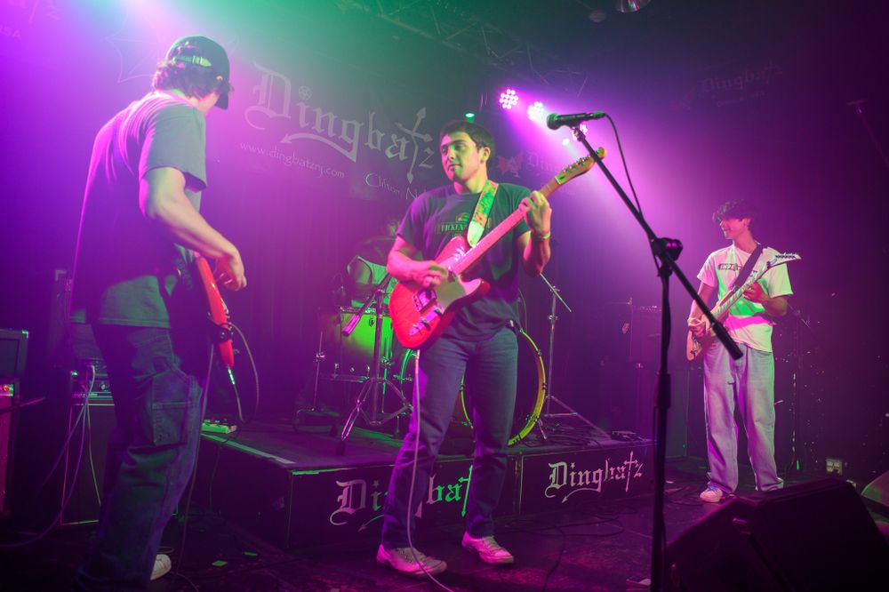 Band performing on stage with colorful pink and green lighting during a live concert at a music venue.