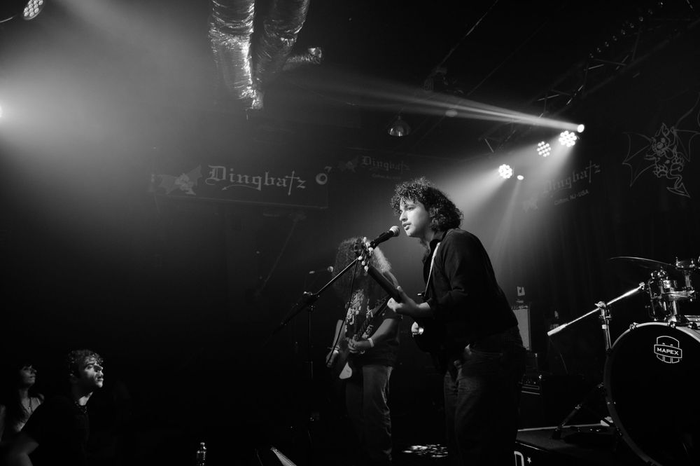 Black and white photo of a performer singing and playing guitar on stage with dramatic spotlights and fog effects.