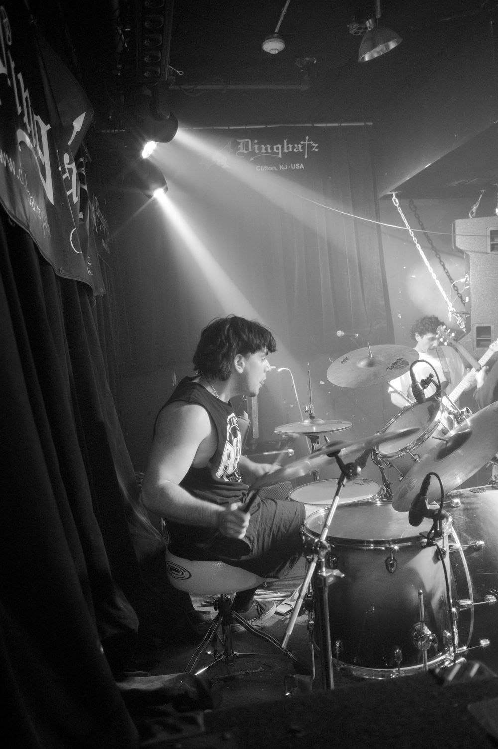 Black and white concert photo showing a drummer performing on stage with dramatic lighting effects.