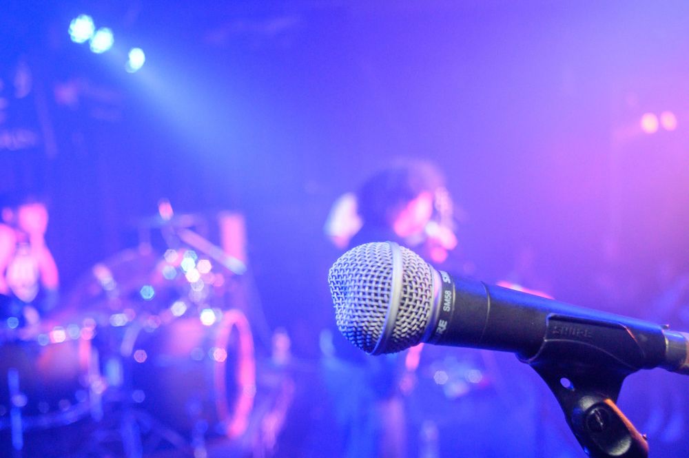 Close-up of microphone on stage with blue stage lights and blurred band members performing in background.