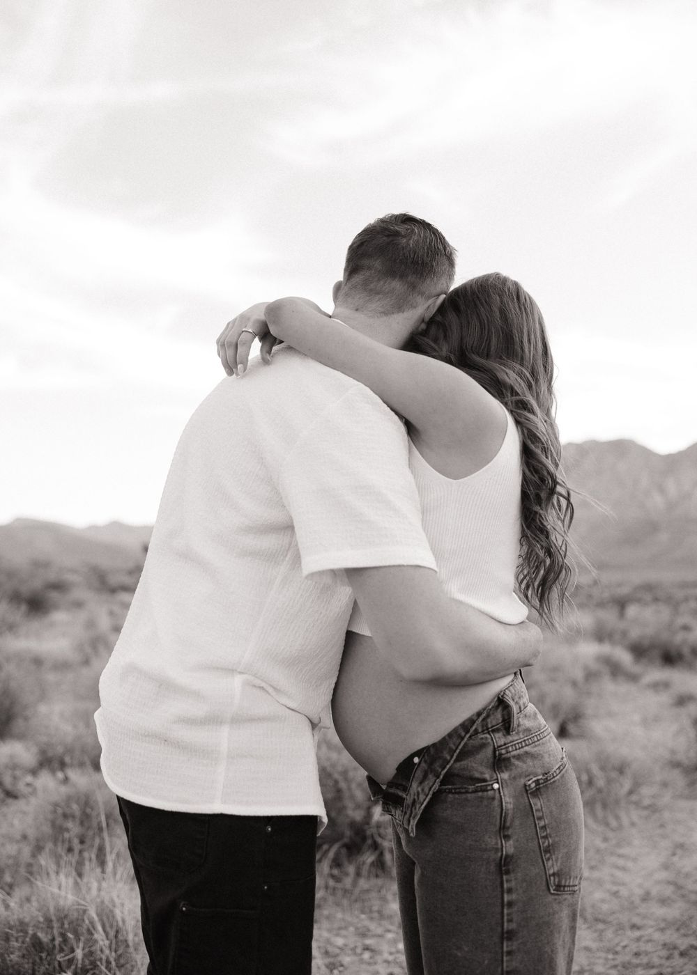 Couple embracing in black and white photo with desert mountains in background.