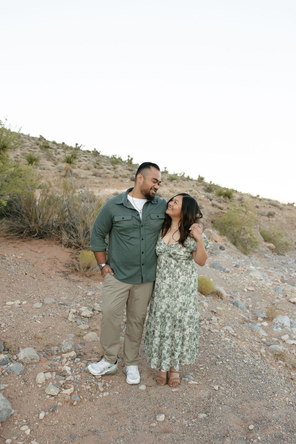 A couple shares a romantic moment while standing on rocky desert terrain during a photo session.