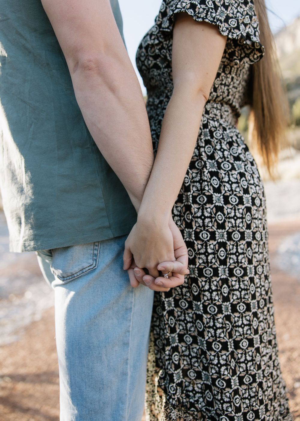 Close up of couple holding hands wearing casual clothing against desert backdrop.
