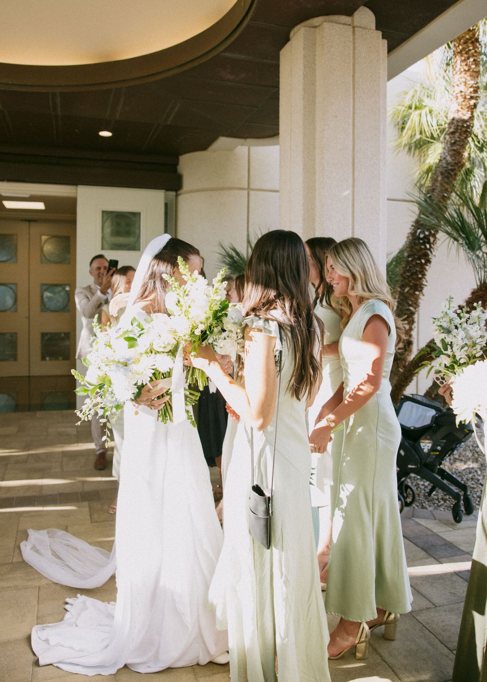 Bride with bridesmaids in soft pastel dresses holding white floral bouquets.