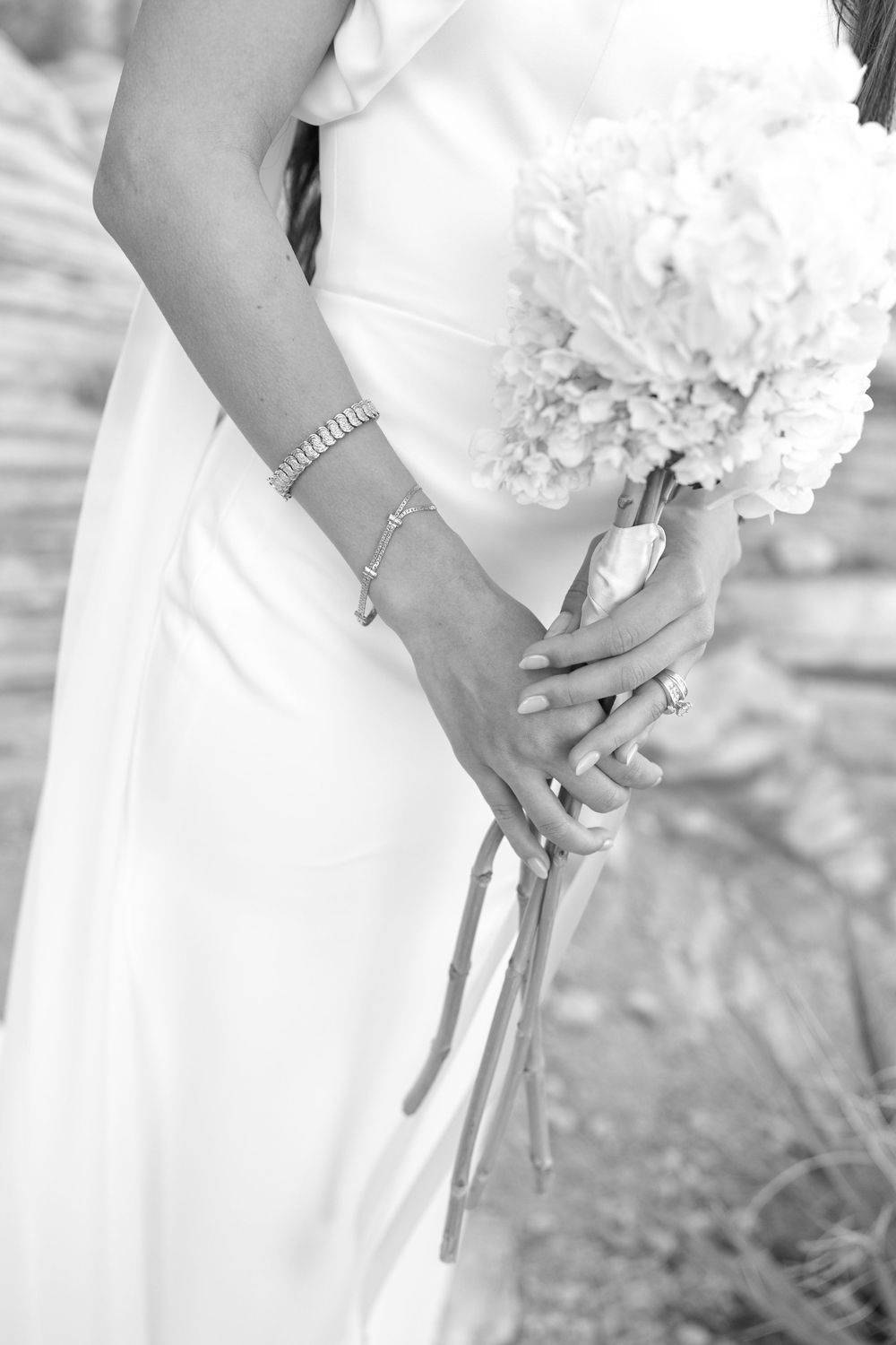 Close-up black and white photo of hands holding white floral bouquets in elegant wedding dresses.