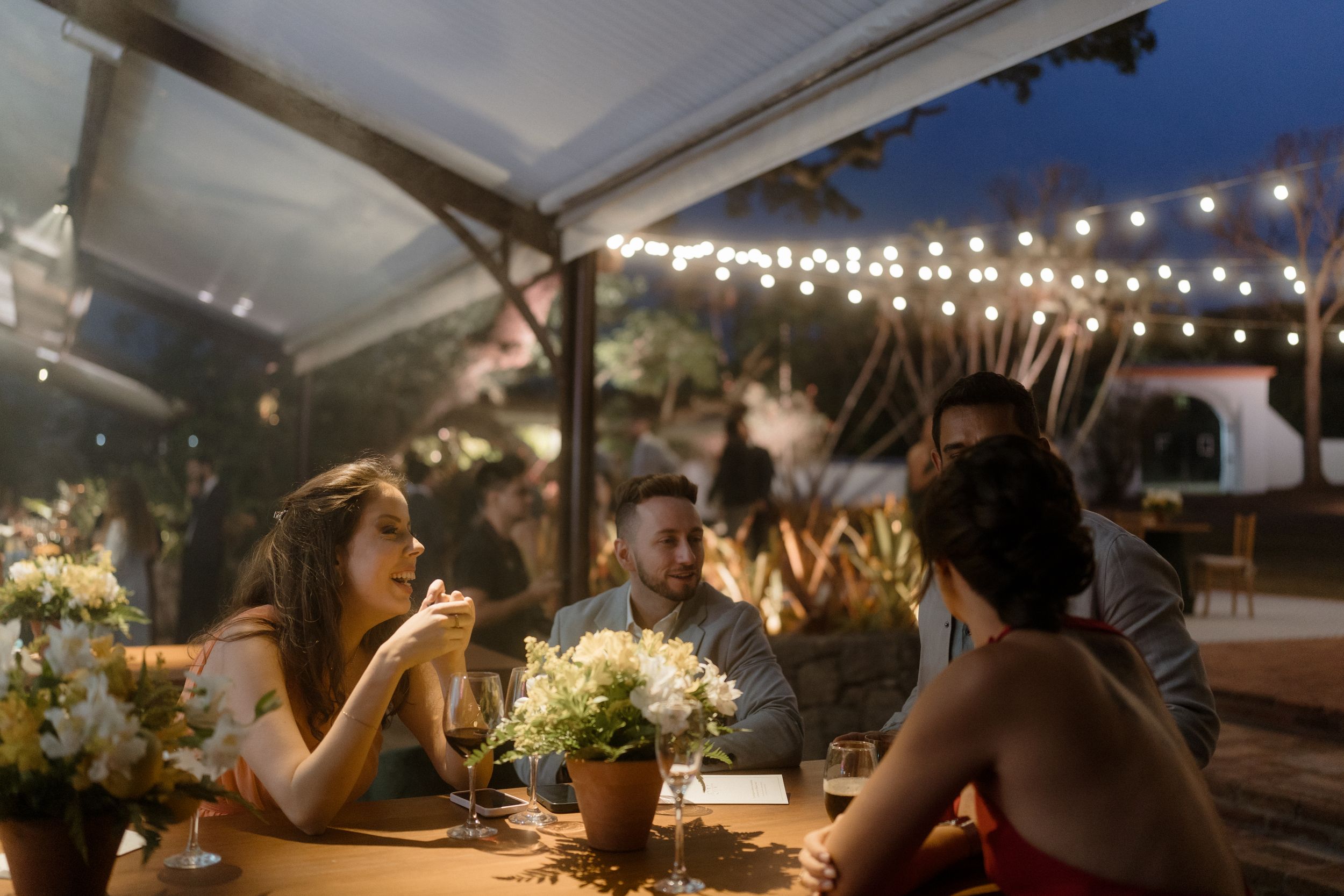 An outdoor wedding reception under string lights with guests enjoying dinner at tables.