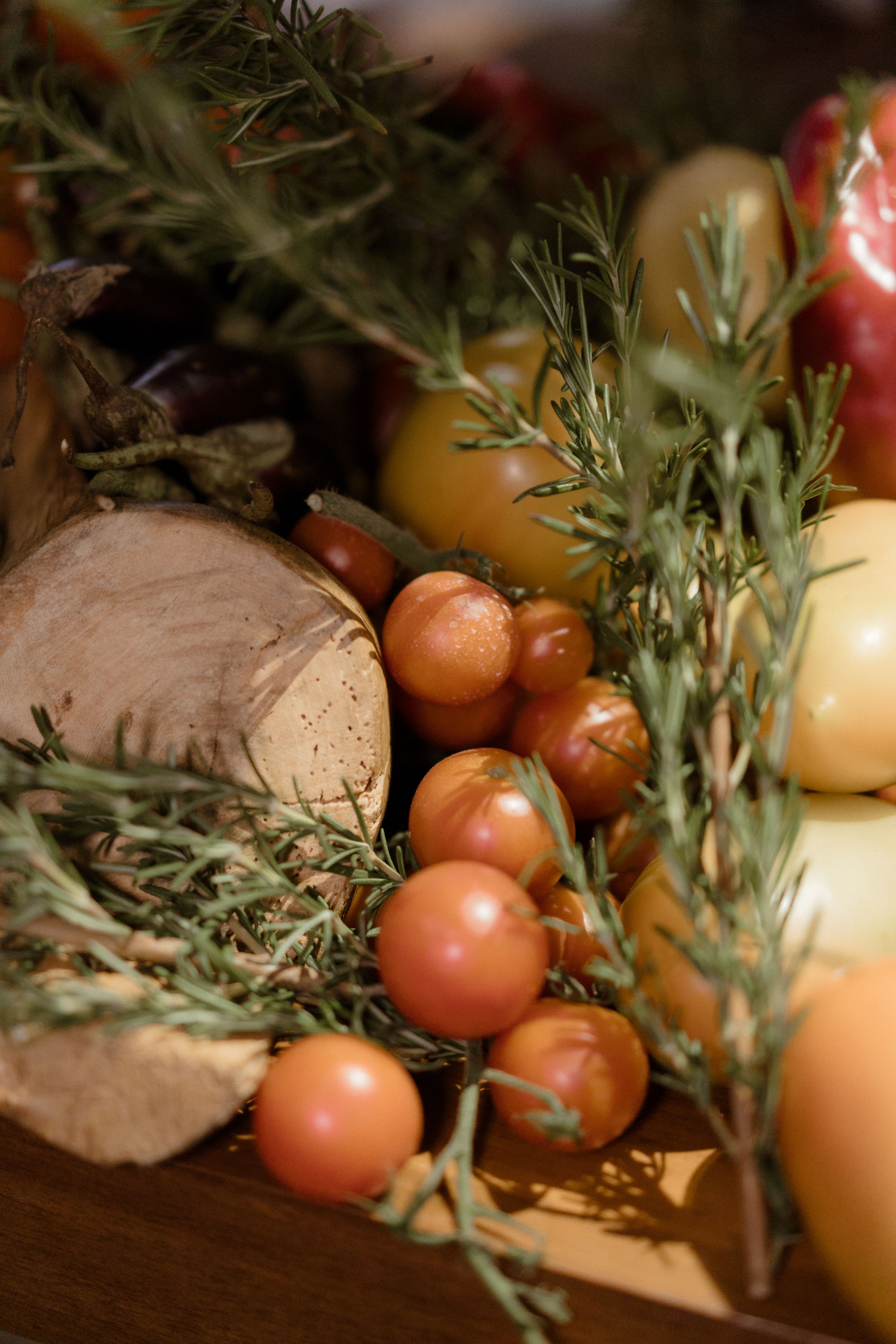Fresh herbs, cherry tomatoes and produce arranged on a rustic wooden surface.