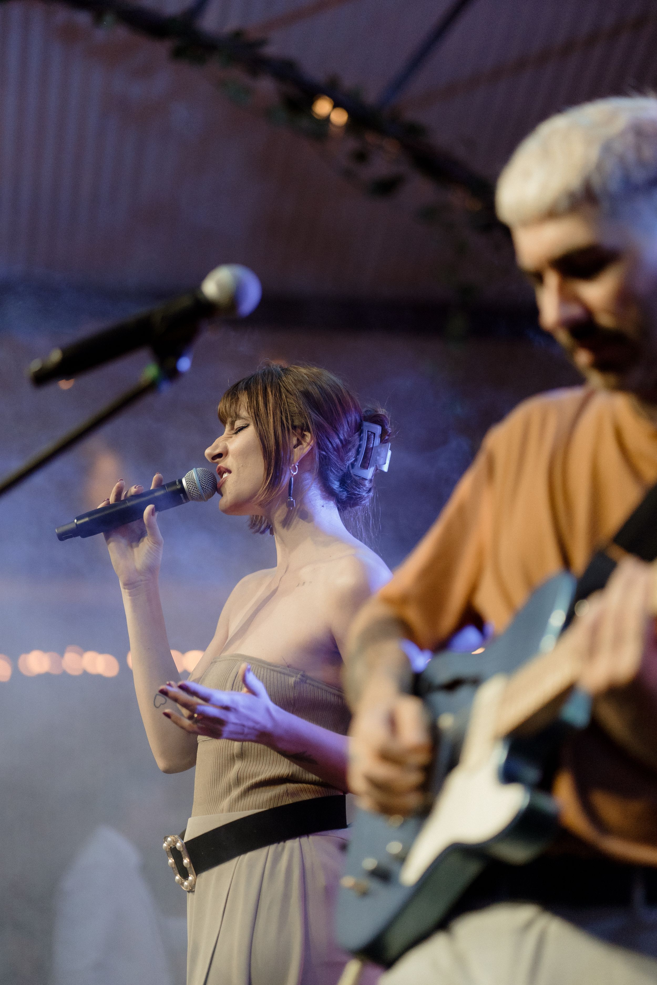Performers on stage singing and playing guitar under concert lighting.