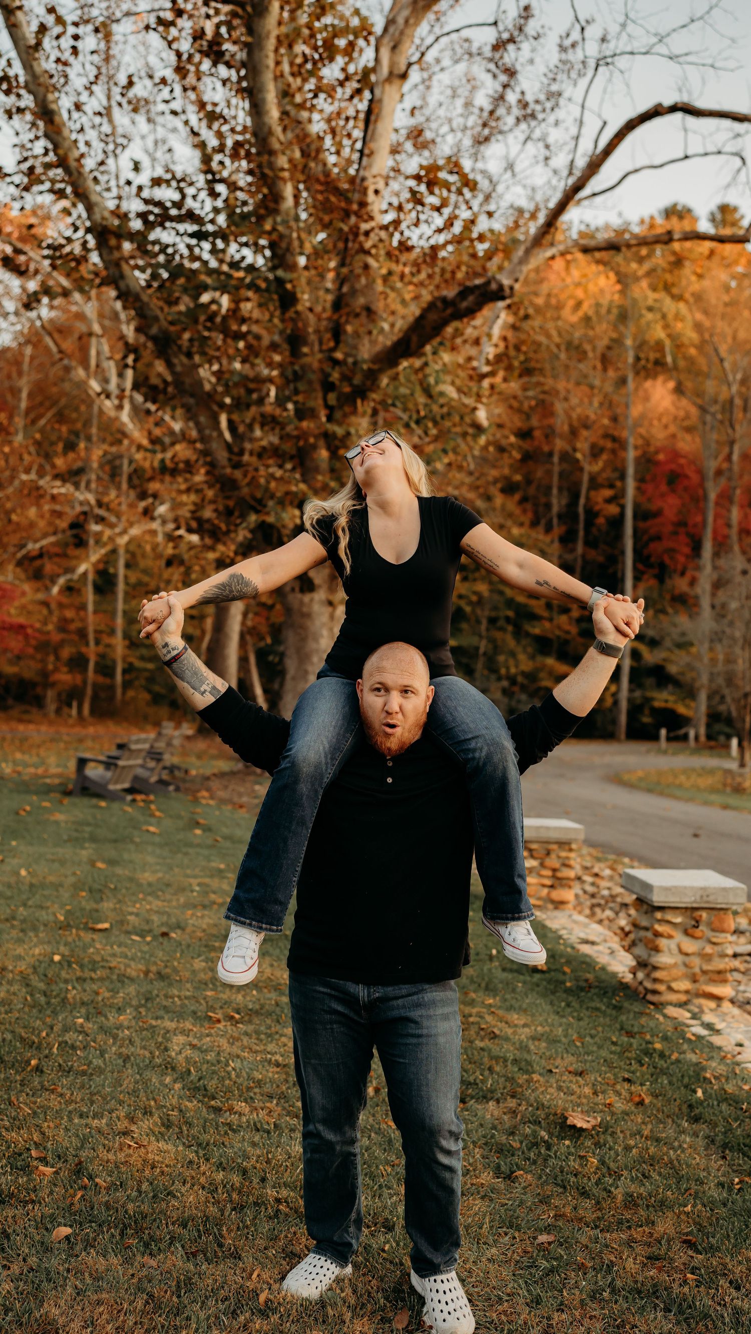Couple having fun with acrobatic pose in front of colorful fall trees in park setting.