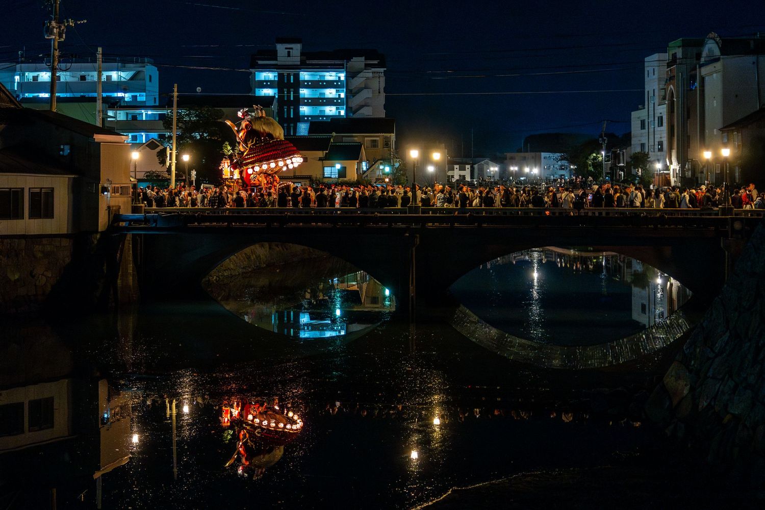 Night scene of illuminated bridge with lanterns reflecting in canal waters.
