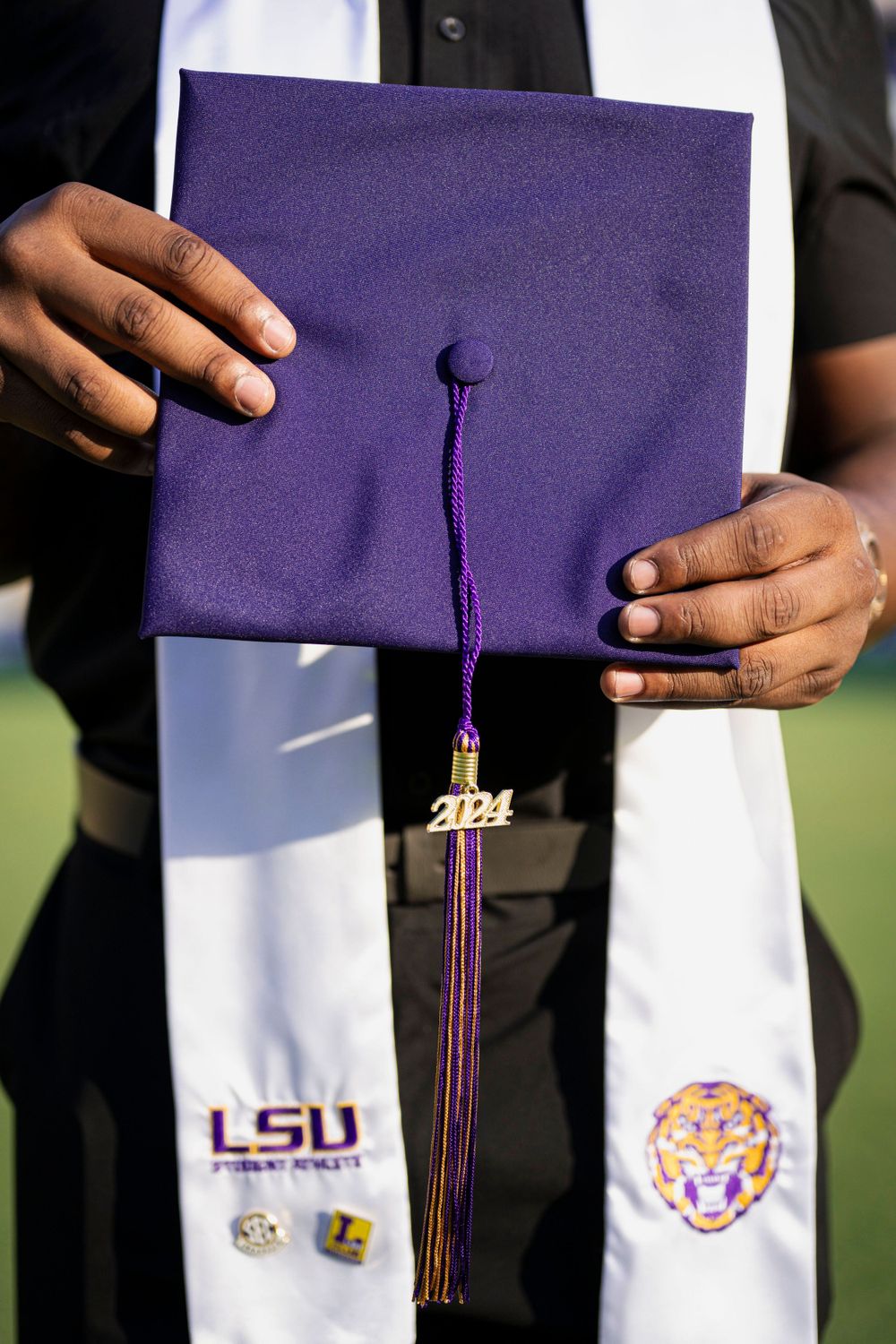 Purple LSU graduation cap with tassel and tiger logo displayed against white stole.