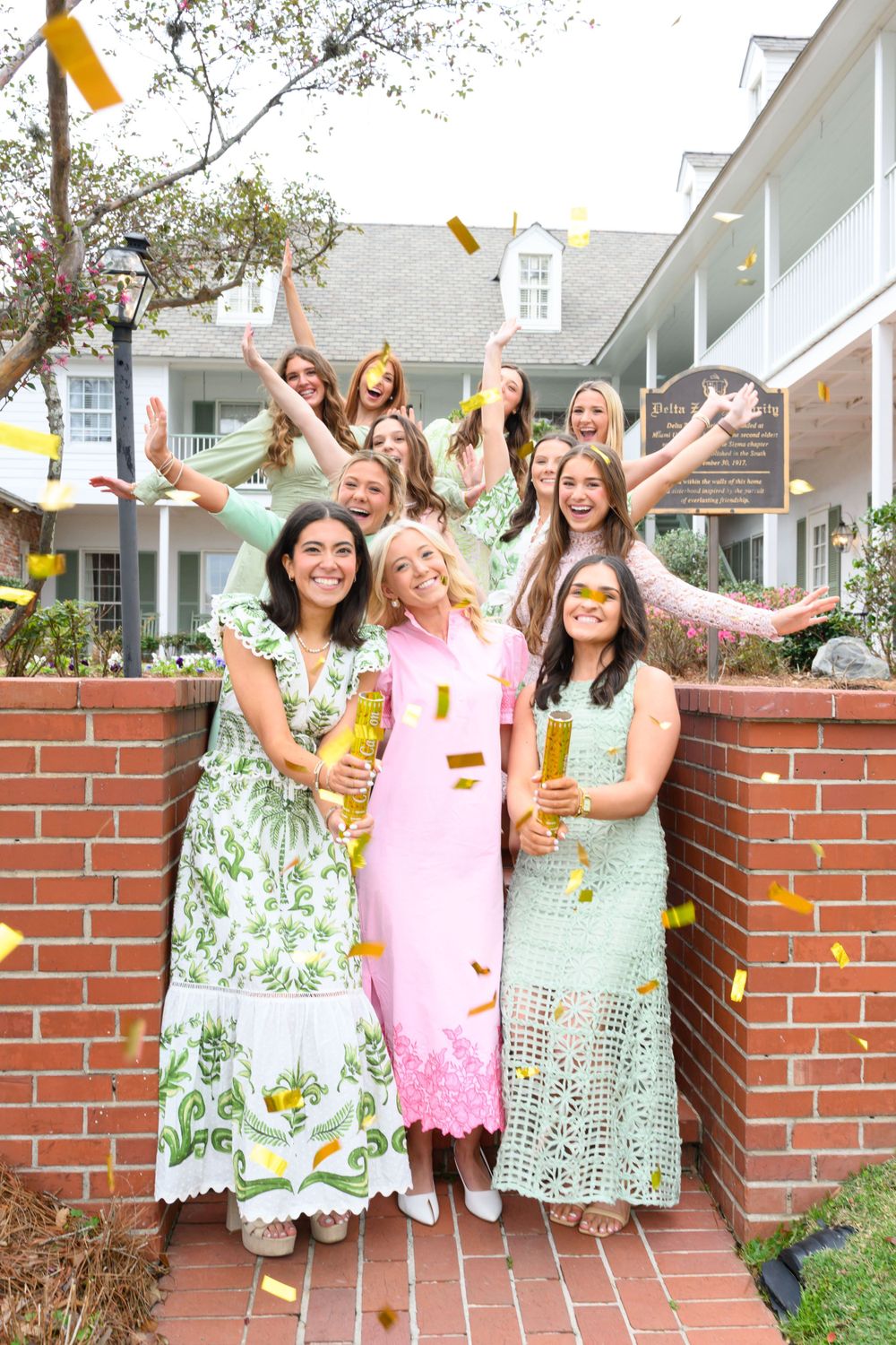 Group of women in spring dresses celebrating with confetti on brick steps.