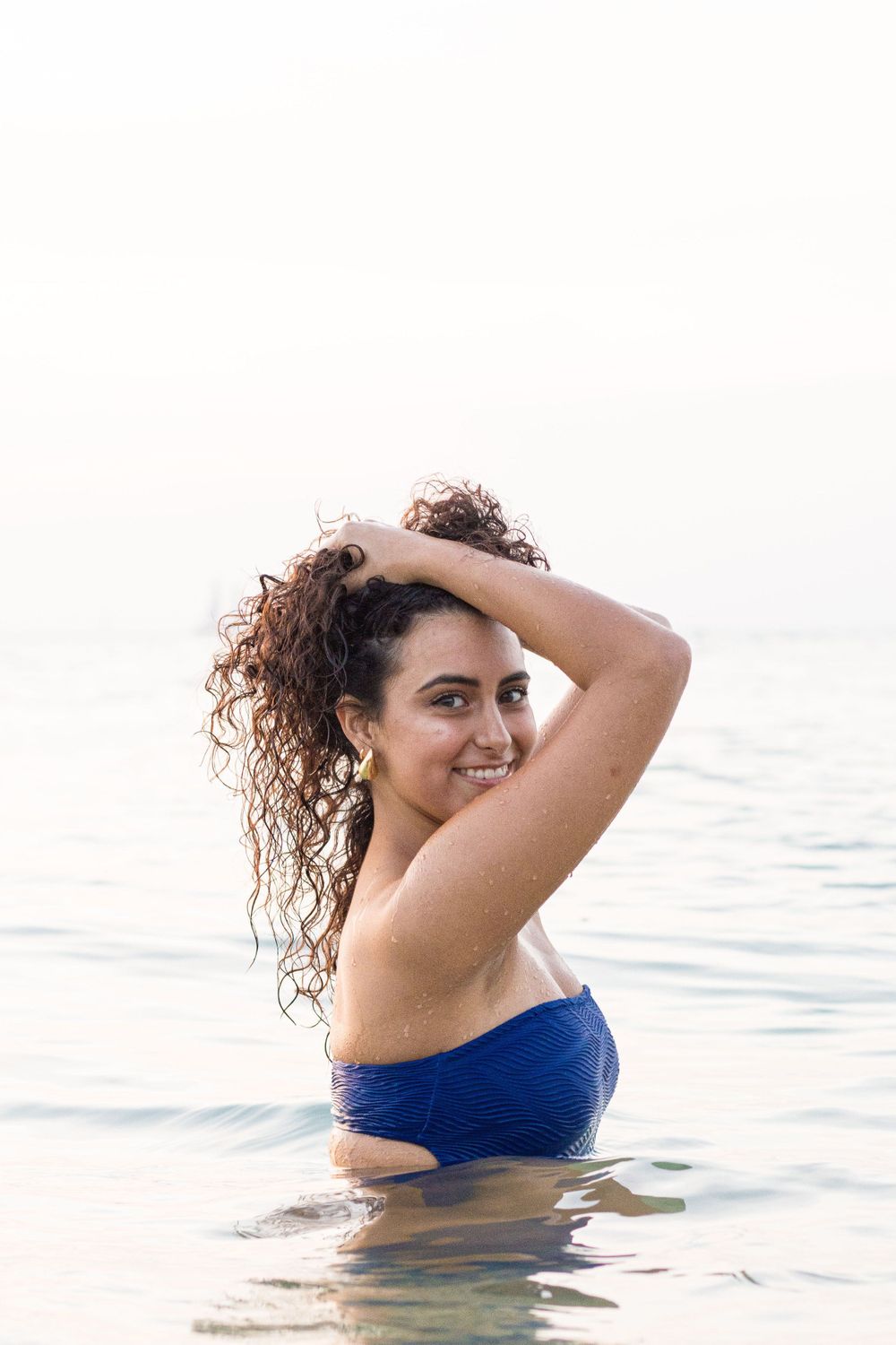A woman in a blue swimsuit enjoying time in calm waters at sunset.