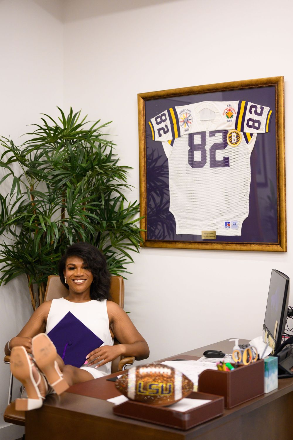 A decorated office with a framed football jersey on the wall and a potted plant near a desk.