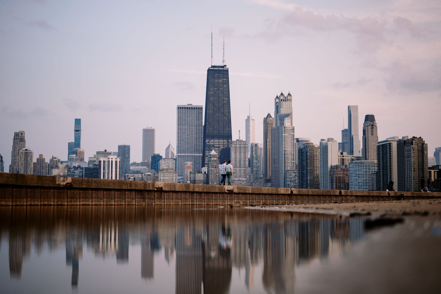 Chicago skyline reflecting in Lake Michigan at dusk with John Hancock Center and other iconic skyscrapers.