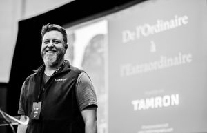 Black and white event photography showing a presenter on stage with projected text.