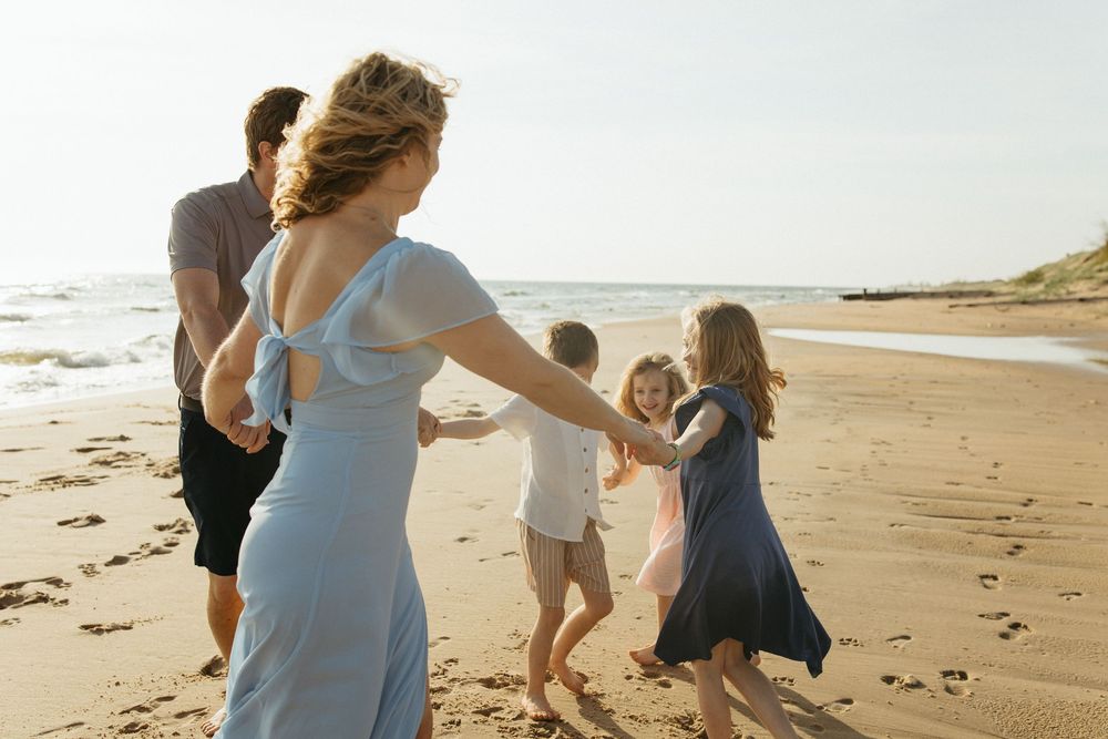 Family holding hands dancing together on a sunny sandy beach near ocean waves on a bright summer day.