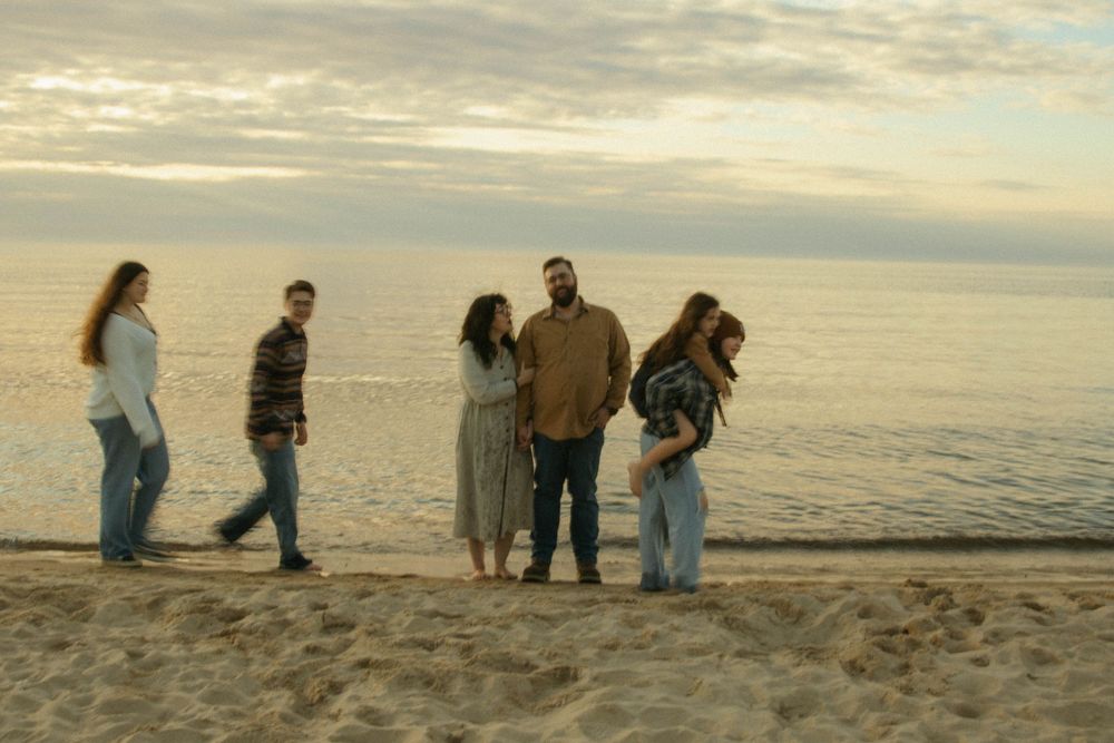 Family of five standing together on a sandy beach at sunset by calm water.