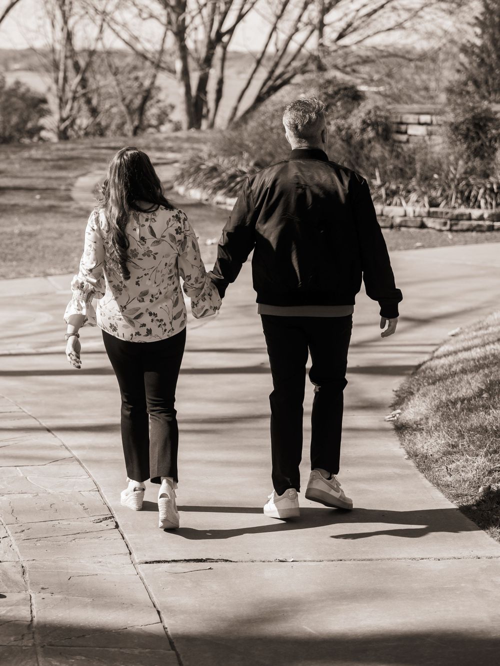 A couple walking hand in hand down a winding path in black and white photography creating a romantic silhouette.