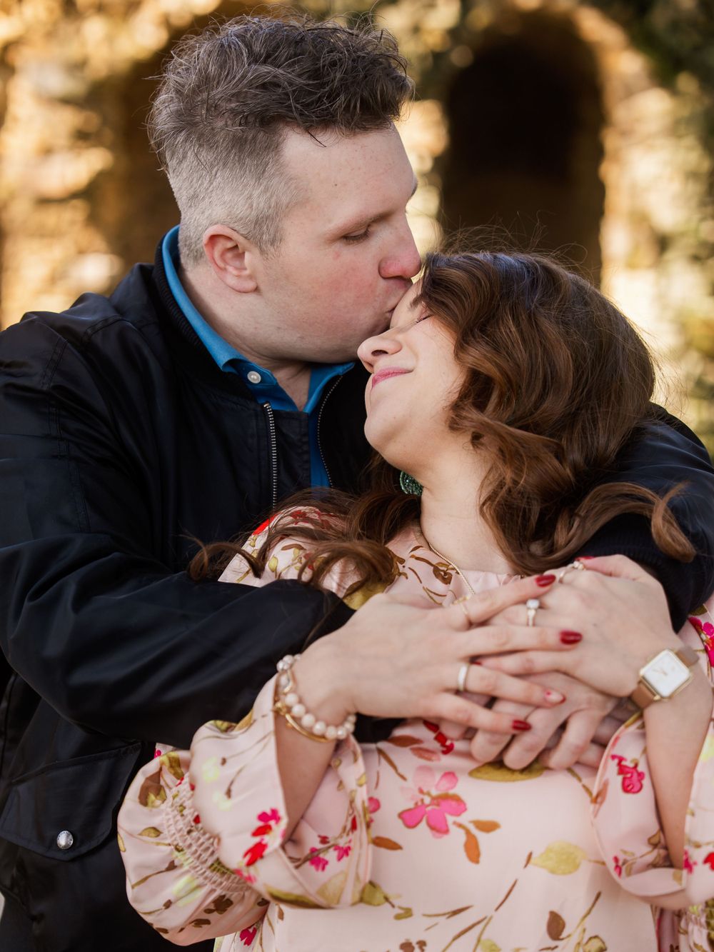 A tender romantic moment captured between two people embracing outdoors with warm sunlit background.