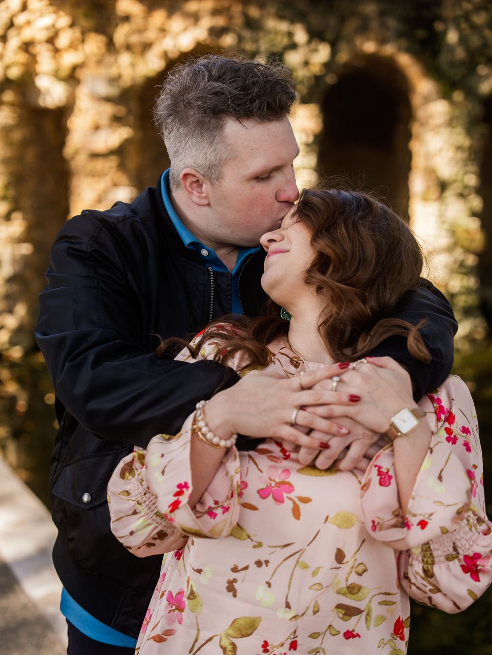 A romantic moment between a couple embracing outdoors with golden sunlight filtering through trees in the background.