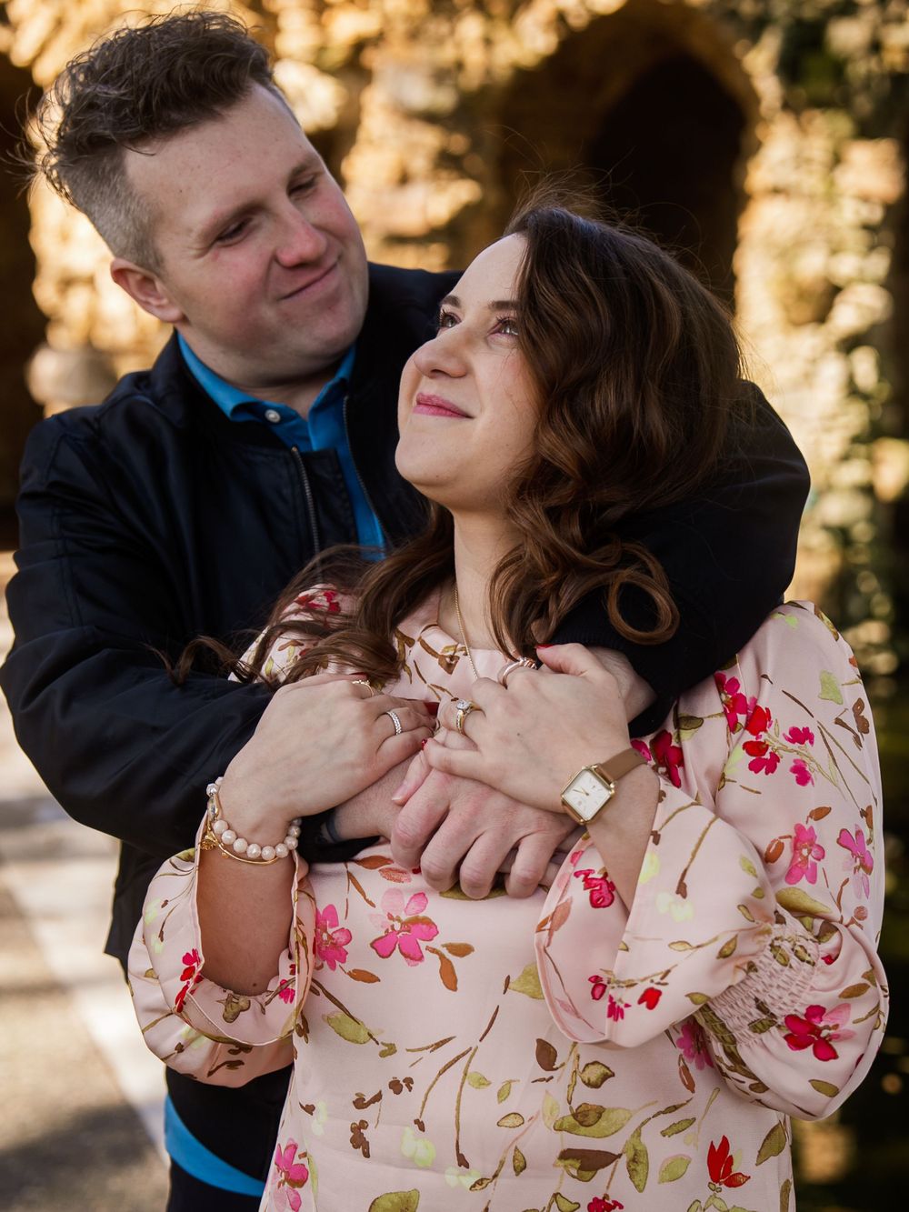 Couple shares a tender moment outdoors in warm sunlight, with person in floral print dress laughing joyfully.