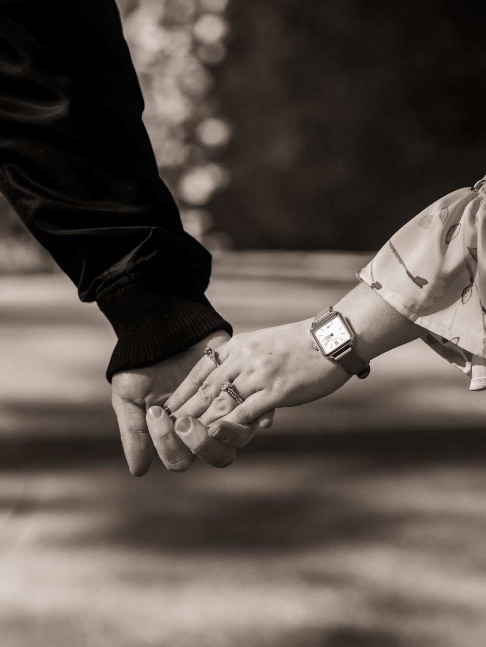 A black and white close-up shot of two people holding hands, with one wearing a smart watch.