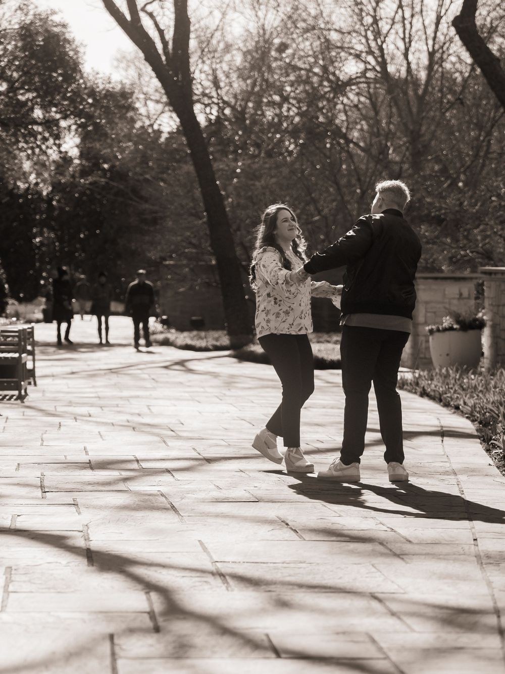 A couple dancing together on a stone path in a park, captured in nostalgic black and white photography.