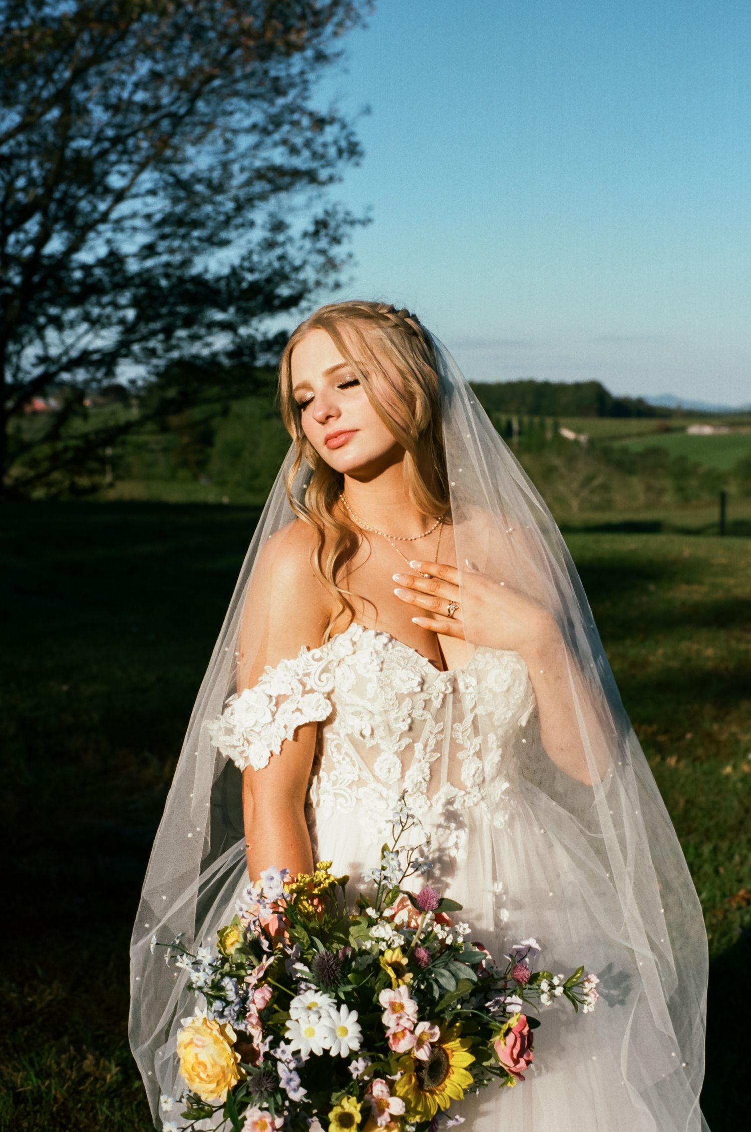 Bridal portrait with colorful bouquet against blue sky and rolling hills backdrop.